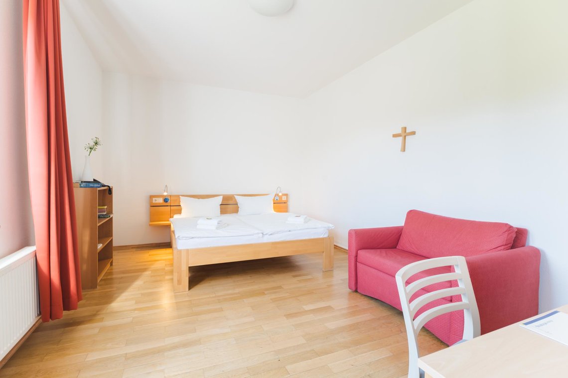 Ein Doppelbett und ein rotes Sofa stehen in einem Raum