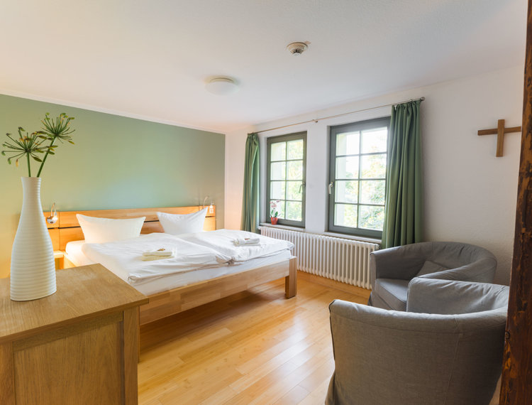 Ein Doppelbett und zwei Sessel stehen in einem Raum mit einer grünen Wand und grünen Gardinen