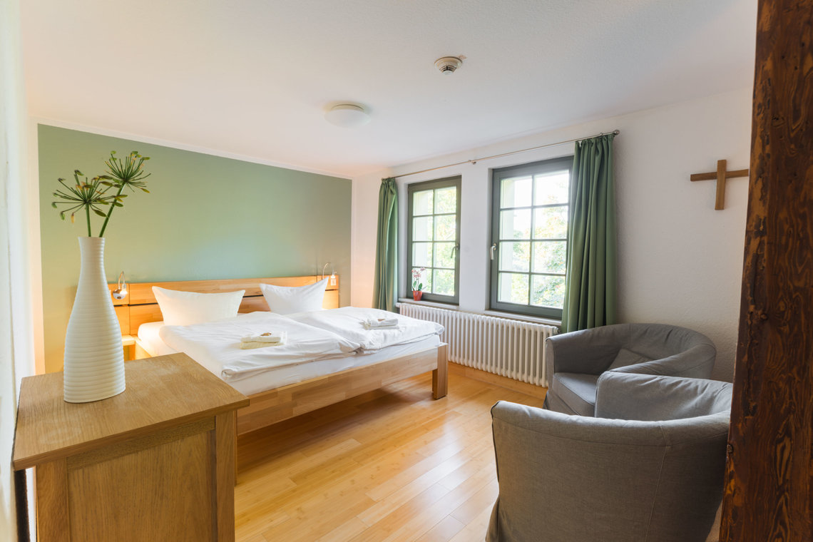 Ein Doppelbett und zwei Sessel stehen in einem Raum mit einer grünen Wand und grünen Gardinen