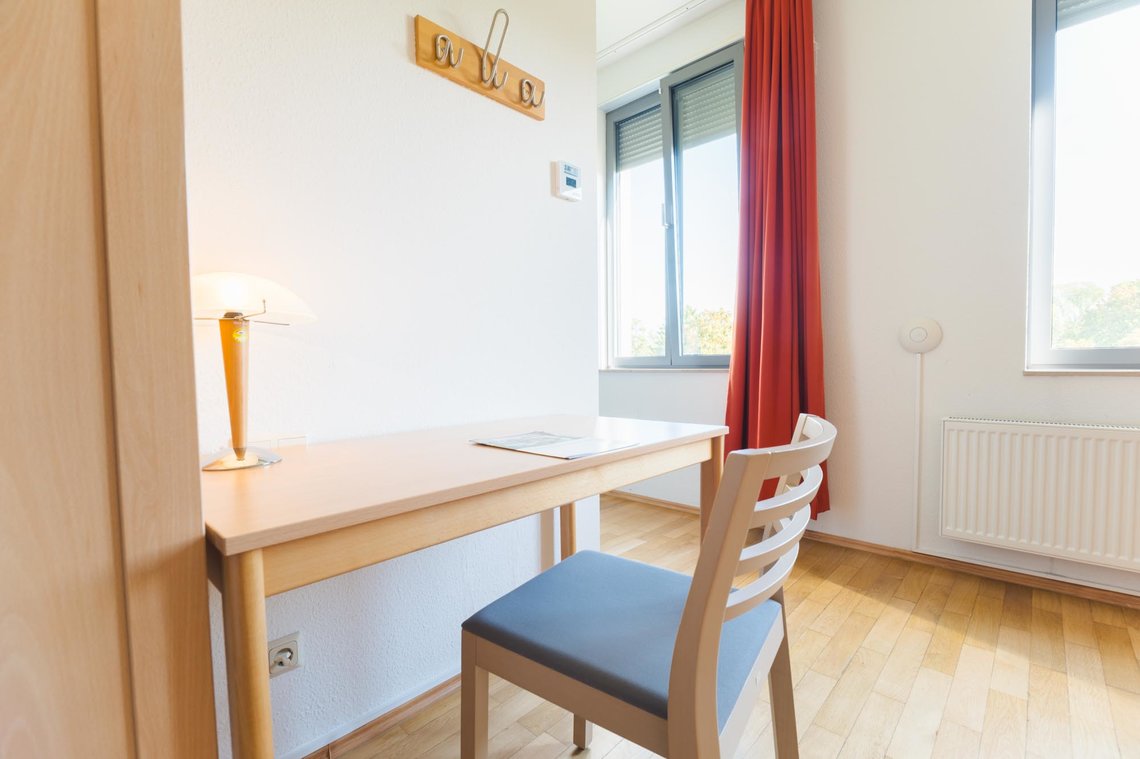 Ein Schreibtisch und ein Stuhl stehen vor einer weißen Wand