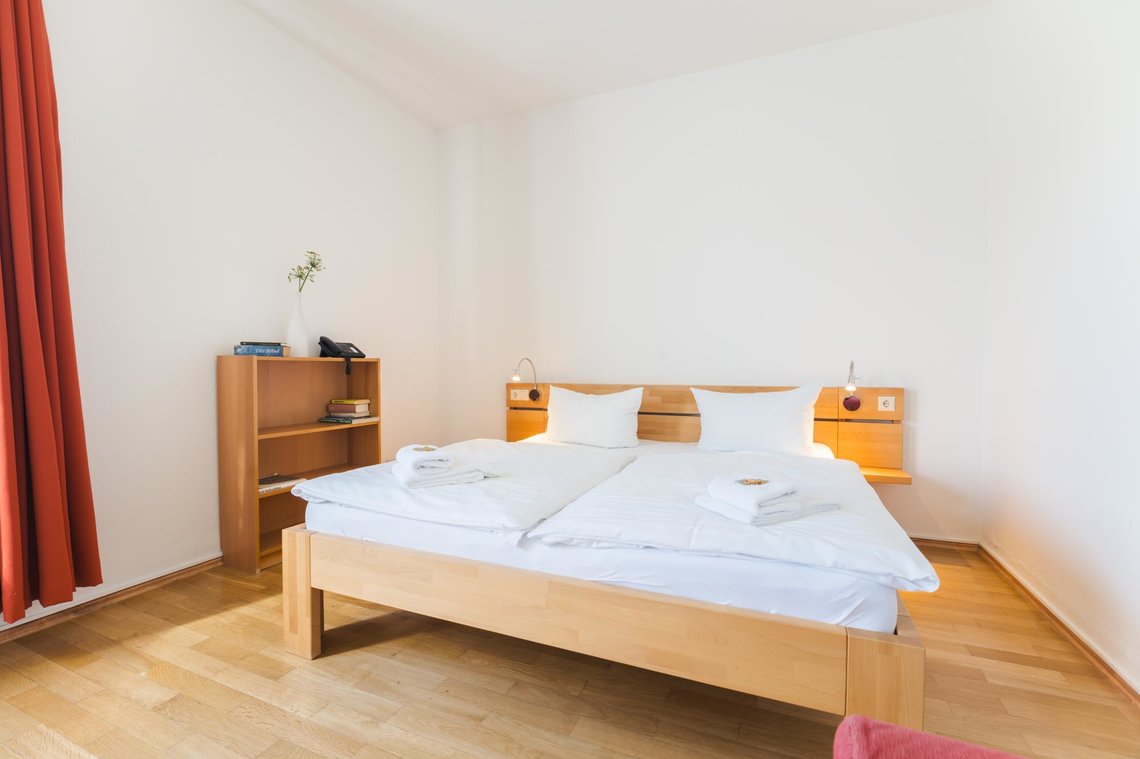 Ein Doppelbett und ein Bücherschrank stehen vor einer weißen Wand