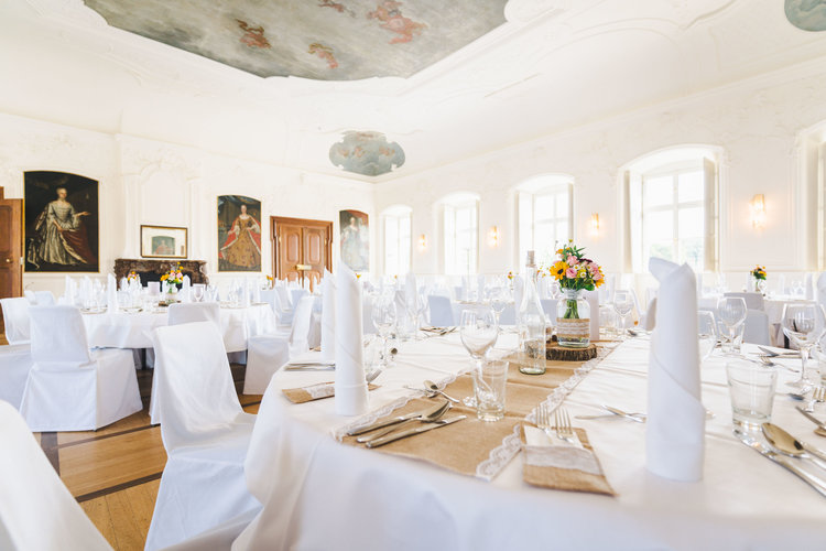 Der große Kaisersaal ist feierlich geschmückt. Die runden Tische sind mit weißen Tischdecken gedeckt und die Stühle in weißen Stoffen gehüllt. Die Tische sind gedeckt mit Besteck, weißen Servietten und einer Blumenvase