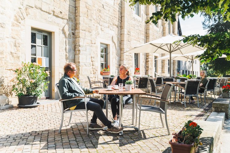 Ein junges Paar sitzt bei Sonnenschein vor dem Klostercafé der Huysburg.